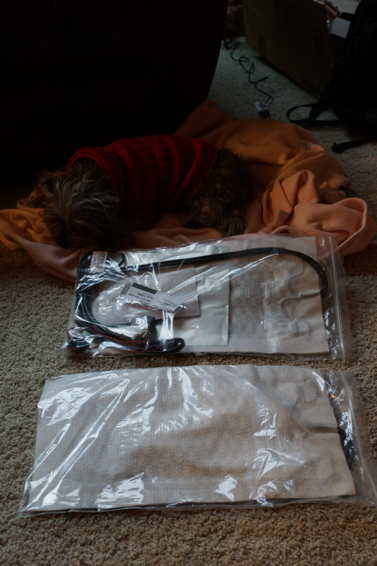 Daisy, lying on a heated dog pad (covered in blanket) next to the two packages from Amazon. Each package contains both a lumbar and butt pad, as well as all the wiring.